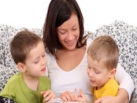 mother and two sons reading book in bed